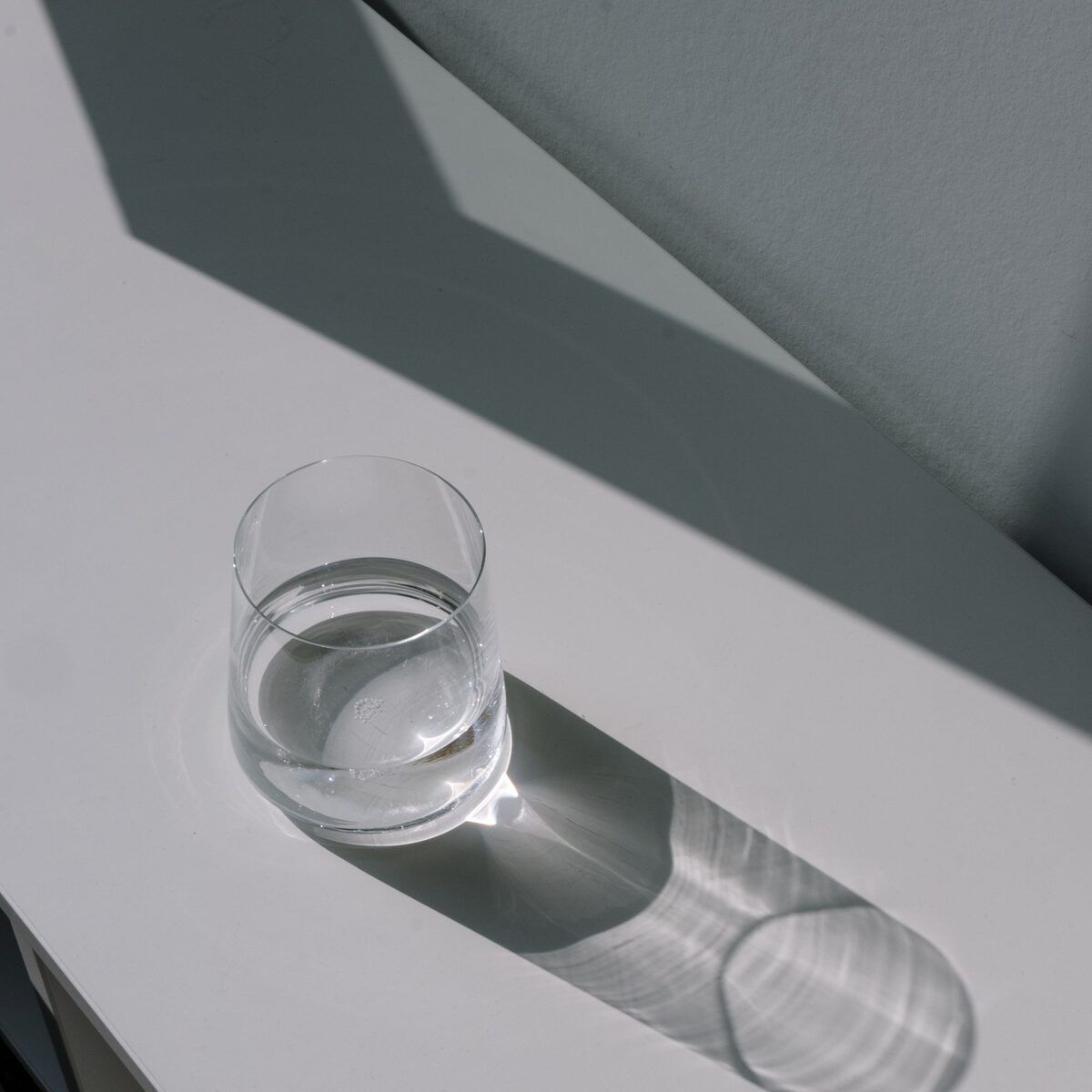 Glass of water casting a long shadow on a white table