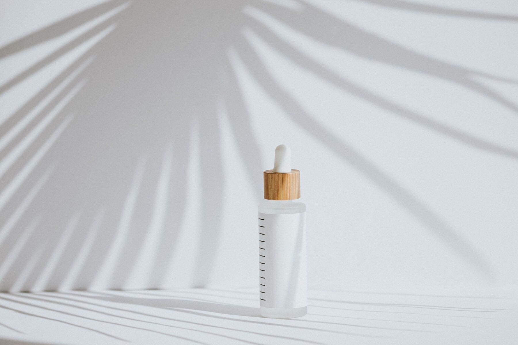 Dropper bottle with a blank label in the shadow of a palm leaf