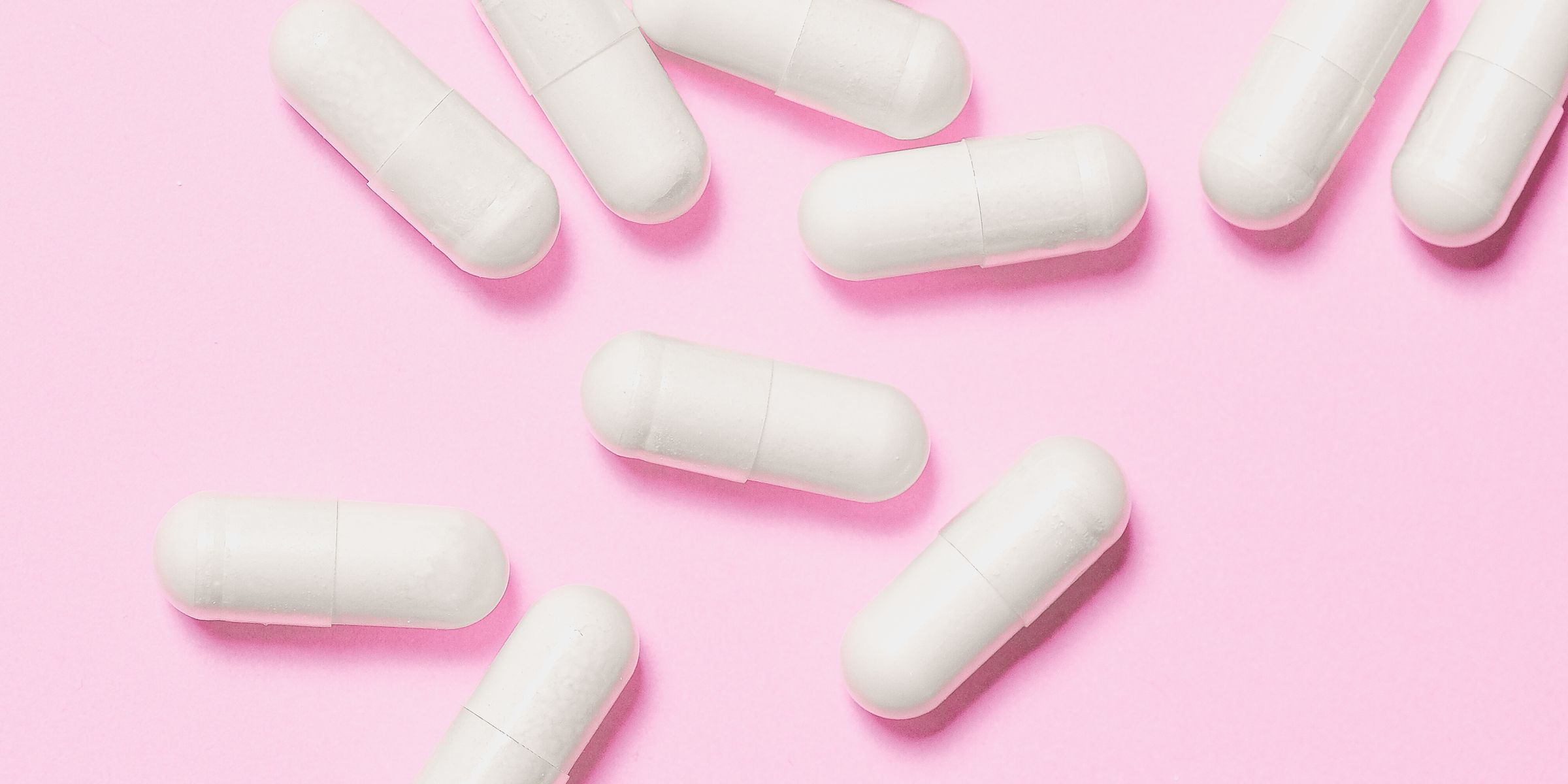 White capsules scattered on a soft pink surface